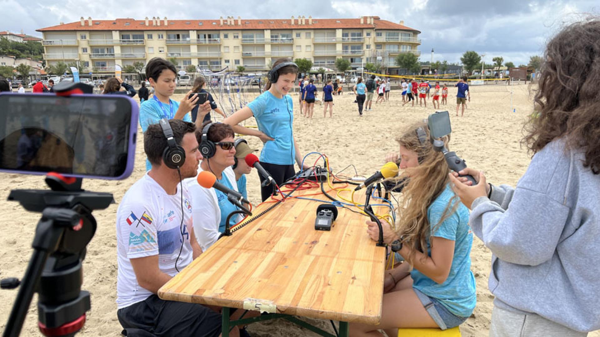 Lors des Jeux internationaux de la jeunesse 2023, une équipe de vingt-six jeunes reporters internationaux a couvert l'événement et produit des contenus en audio, vidéo, photo ou encore par écrit. Ici, un studio de web-radio mobile a été installé sur la plage des Sables d'or à Anglet, qui a été le théâtre des plusieurs activités (sandball, beach-relais, volley-ball et démonstration de sauvetage côtier) pour recueillir les propos des participants.